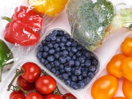 An assortment of fresh vegetables and fruits, including red and yellow bell peppers, broccoli, cherry tomatoes, and blueberries, arranged in a plastic container.