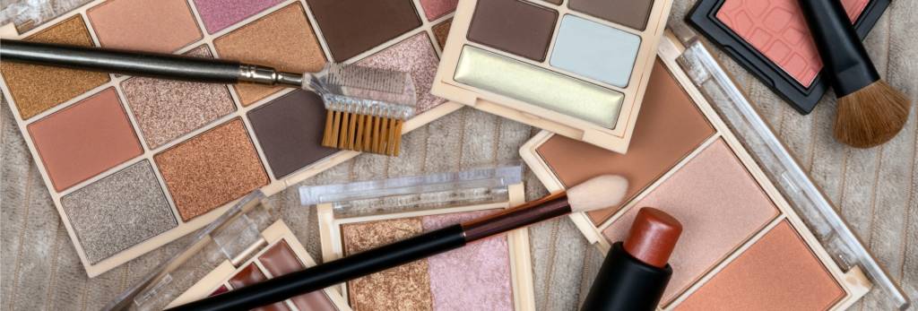 A variety of makeup palettes and brushes arranged on a textured surface, showcasing different shades of eyeshadow, blush, and highlighter.